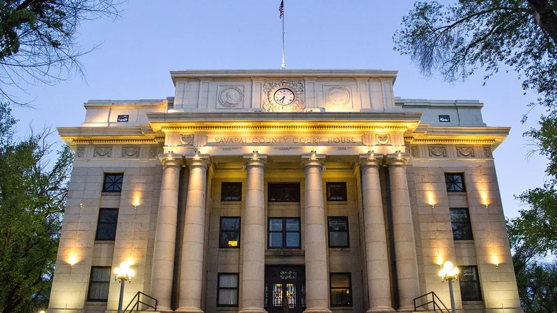 The columned Yavapai County Courthouse lit up at dusk, framed by trees on the Courthouse Plaza in downtown Prescott